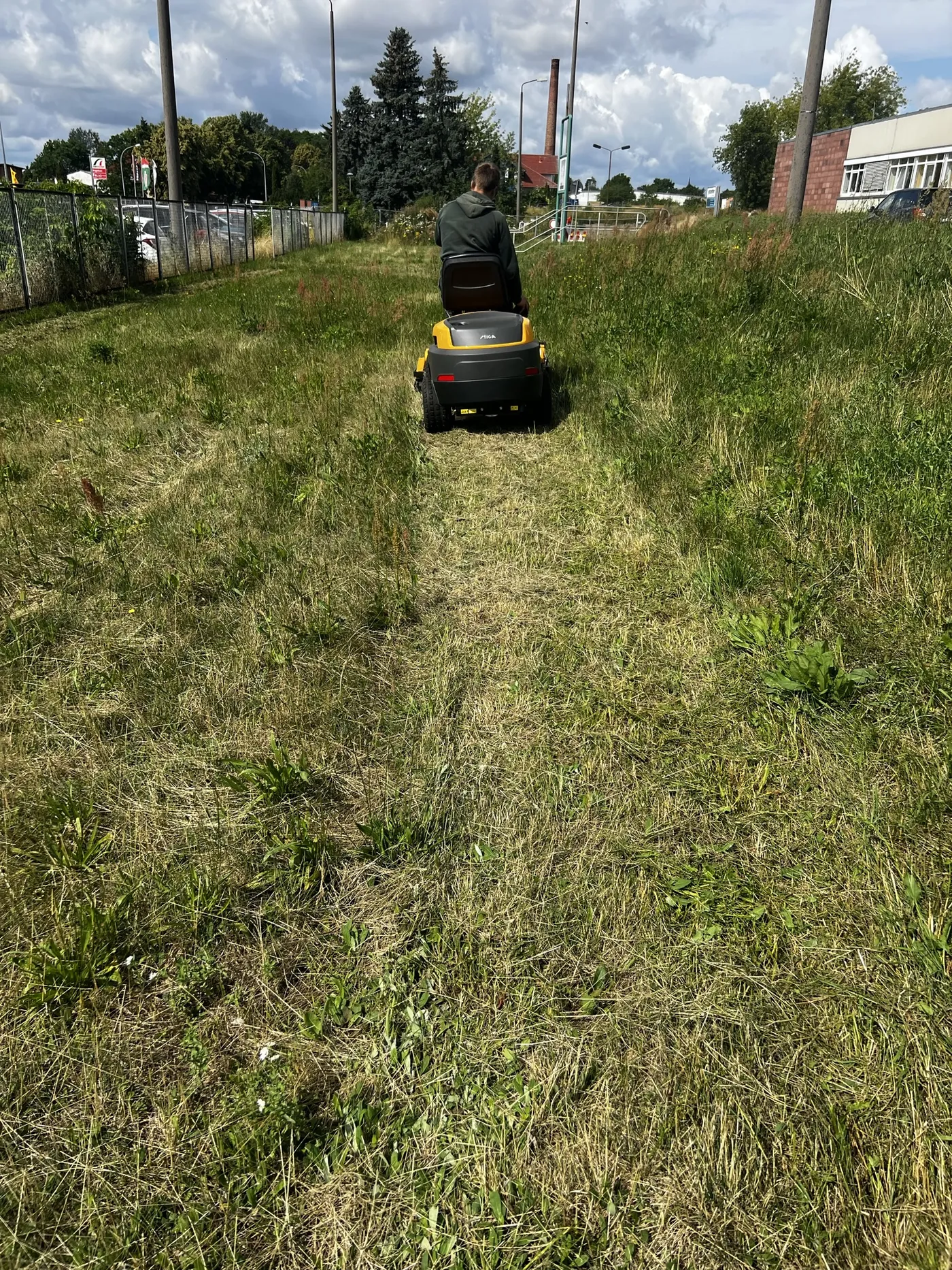 Grünpflege – Aufsitzmäher bei der Rasenpflege an Gebäude