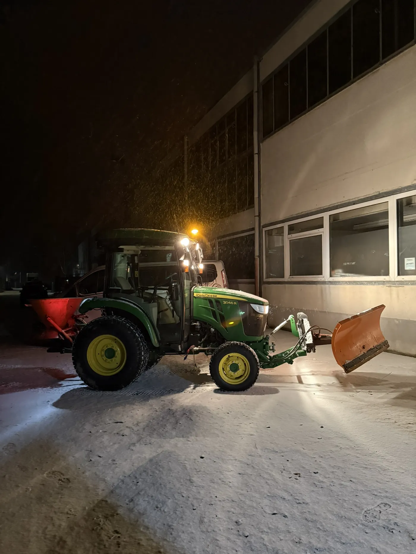 Winterdienst – John Deere Traktor mit Schneeschild räumt Parkplatz bei Nacht